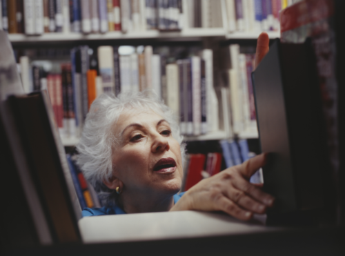 mature woman placing a book on a library shelf