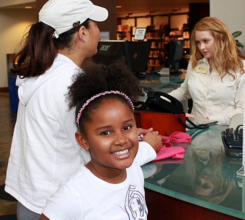 A girls smiles at the camera while standing at a library circulation desk