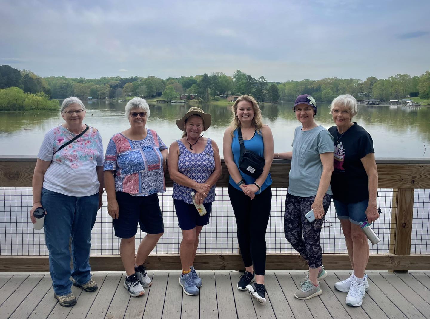 Six smiling people wearing walking shows and standing on a deck in front of a lake