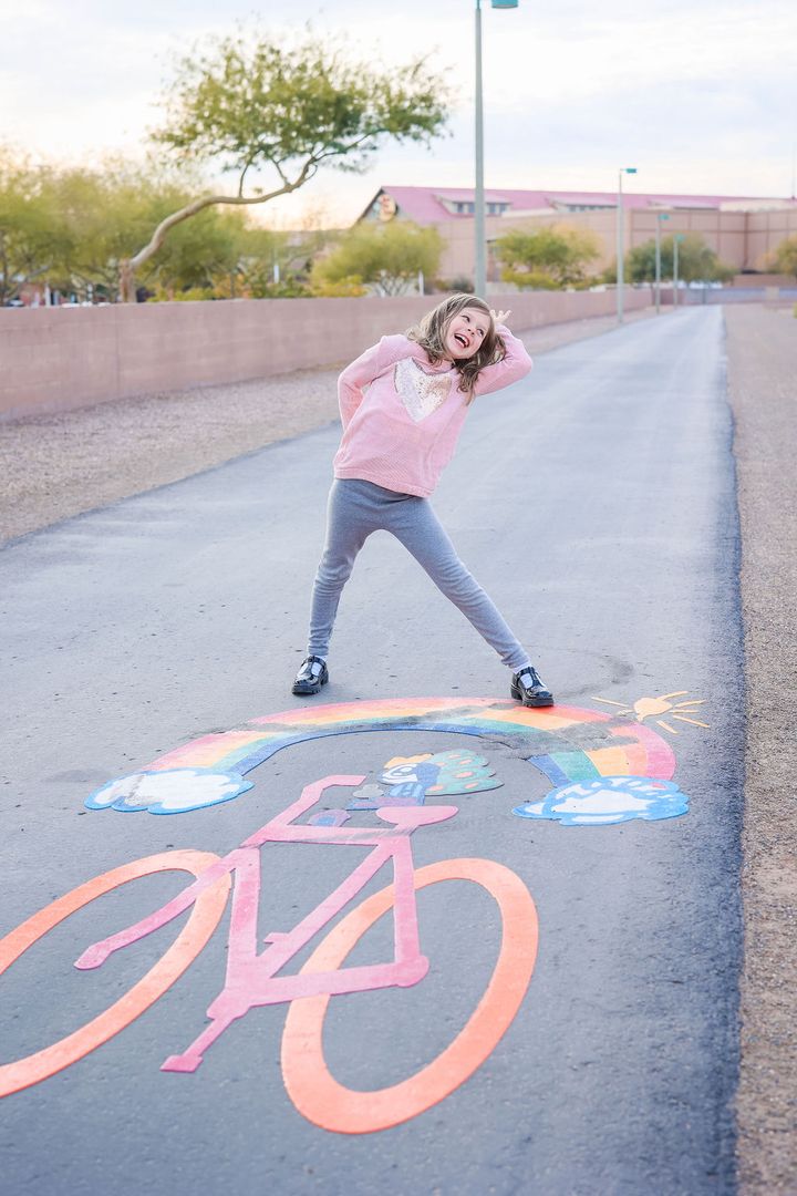 Young smiling girl standing in front of a bike logo on a bike path