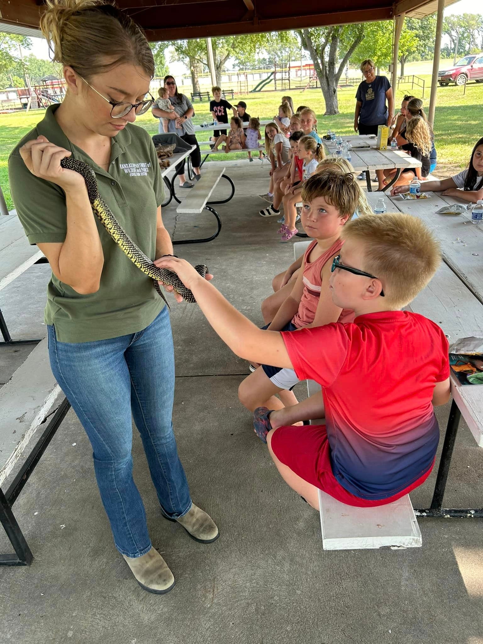 Woman showing a snake to a group of children sitting at a picnic table in a shelter house