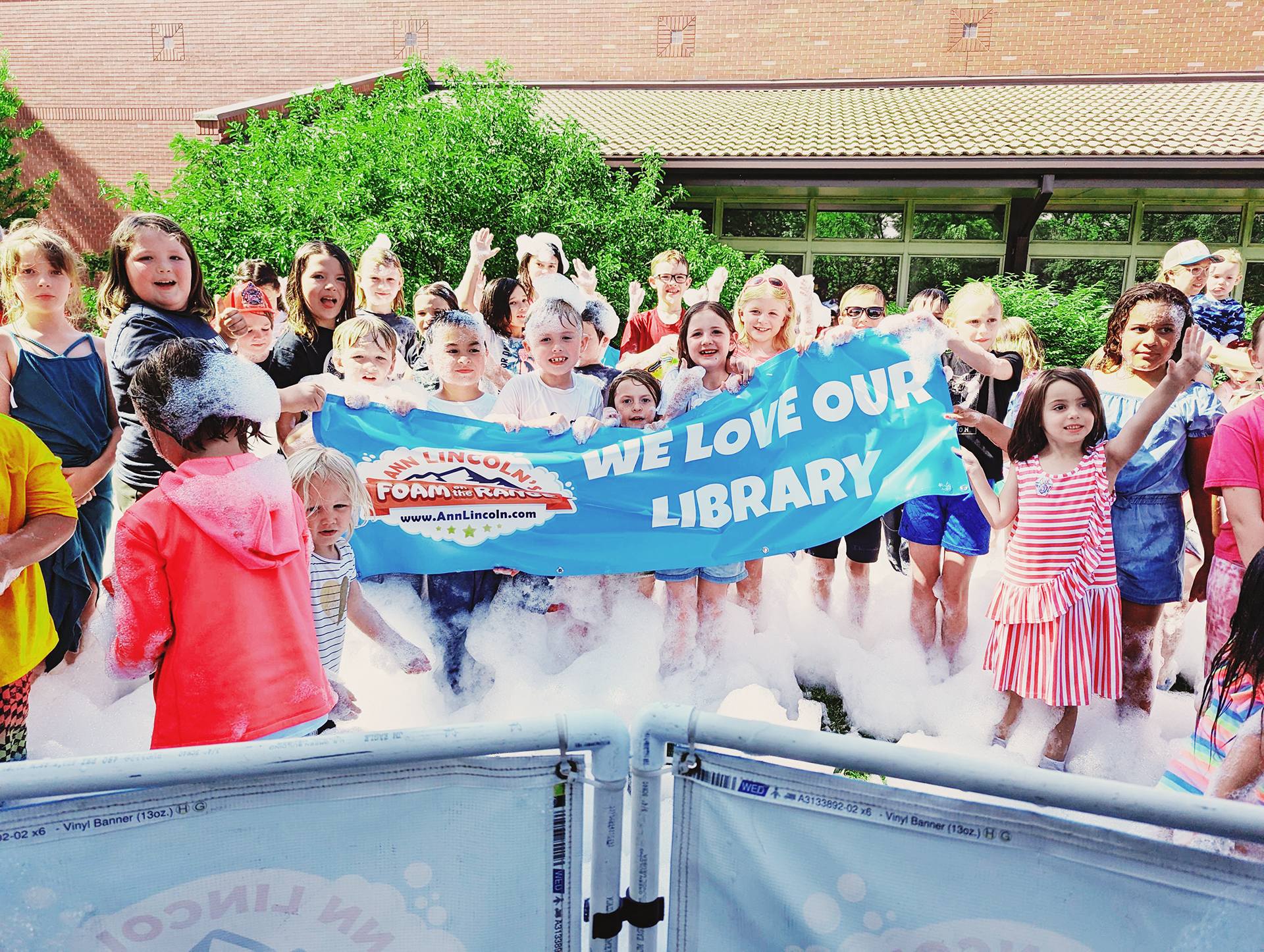 Large group of children standing in bubbles and holding a sign that reads ‘We love our library’