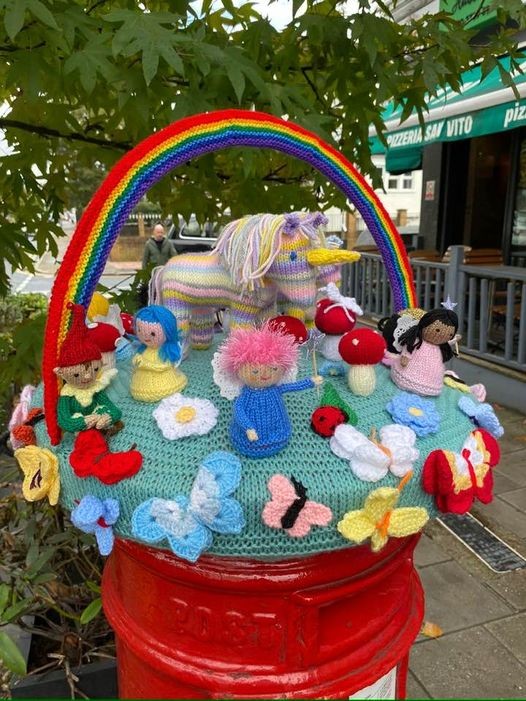 Beckenham Knit and Knatter project Close-up image of a group of colorful, fantastical knitted creatures sitting under a rainbow atop a fire hydrant
